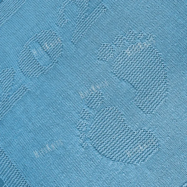 Minimalist knitted baby blanket with “2025” and baby feet motif in textured garter stitch on a smooth stockinette background, finished with a wide garter stitch border. Neutral blue newborn blanket design for stroller, nursery, baby shower gift, or pregnancy announcement photo prop.