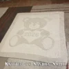 Beige knitted baby blanket featuring a textured teddy bear holding a heart with “2026” inside. The teddy bear and border are worked in raised garter stitch against a smooth stockinette background, creating a soft embossed effect. Handmade-style nursery blanket design for newborn babies and baby shower gifts.