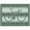 Knitted blanket featuring a bicycle motif in the center, worked in garter stitch against a stockinette background. The blanket has a textured border framing the bike design. The bicycle is shown in a side profile with detailed wheels, frame, handlebars, and pedals, suitable for cyclists, bike lovers, teens, and adults.