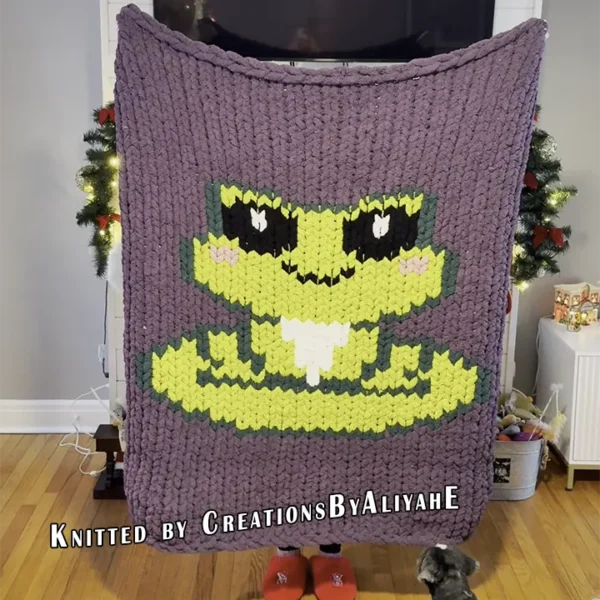 Cute frog chunky knit blanket with pixel art frog design on a lavender background. Finger knitting and jumbo yarn pattern suitable for nursery décor, kids’ blankets, cozy room accents, and handmade gifts.