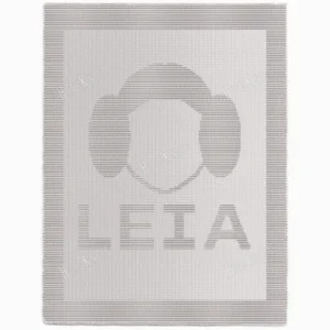 Minimalist knitted blanket featuring a stylized Princess Leia face silhouette with her iconic side buns and the word “LEIA” below. The design is worked in textured garter stitch against a smooth stockinette background, all in a soft neutral color palette with a wide garter stitch border. A modern and cozy blanket design inspired by classic sci-fi themes, perfect for kids’ rooms, reading nooks, movie nights, and Star Wars fans of all ages.