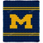 Michigan varsity style chunky knit blanket featuring a bold yellow letter M on a deep blue background with sporty stripe accents, handmade with plush jumbo chenille yarn in a cozy finger knitting graphghan design.