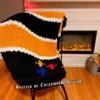 Chunky knit striped blanket inspired by Pittsburgh Steelers football colors, featuring bold black and gold horizontal stripes with white accent lines on a soft plush textured background. The lower corner includes the classic three-diamond symbol in yellow, red, and blue.