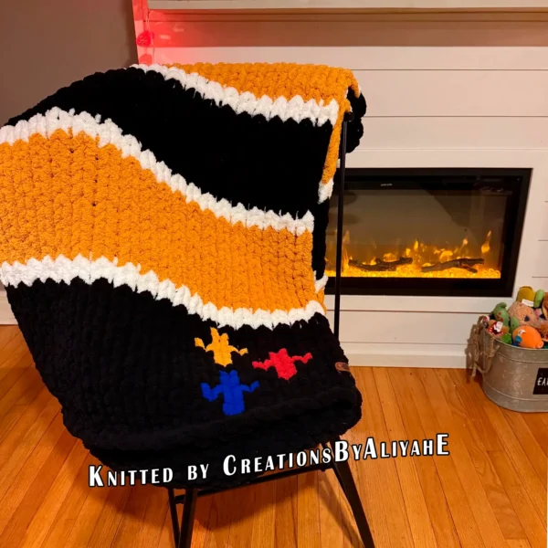 Chunky knit striped blanket inspired by Pittsburgh Steelers football colors, featuring bold black and gold horizontal stripes with white accent lines on a soft plush textured background. The lower corner includes the classic three-diamond symbol in yellow, red, and blue.