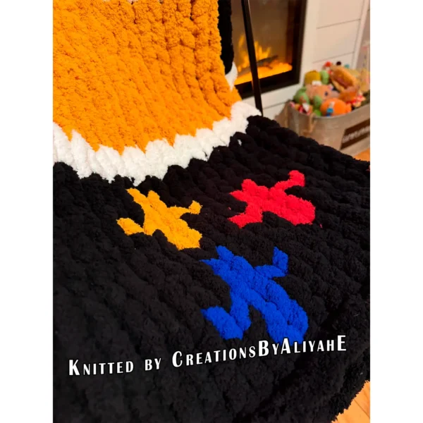Chunky knit striped blanket inspired by Pittsburgh Steelers football colors, featuring bold black and gold horizontal stripes with white accent lines on a soft plush textured background. The lower corner includes the classic three-diamond symbol in yellow, red, and blue.