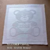 Gray knitted baby blanket featuring a textured teddy bear holding a heart with “2026” inside. The teddy bear and border are worked in raised garter stitch against a smooth stockinette background, creating a soft embossed effect. Handmade-style nursery blanket design for newborn babies and baby shower gifts.