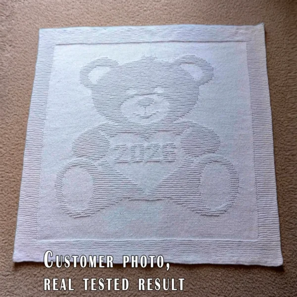 Gray knitted baby blanket featuring a textured teddy bear holding a heart with “2026” inside. The teddy bear and border are worked in raised garter stitch against a smooth stockinette background, creating a soft embossed effect. Handmade-style nursery blanket design for newborn babies and baby shower gifts.