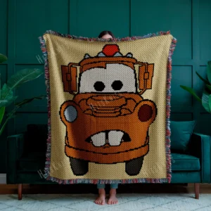 Large C2C crochet blanket featuring Tow Mater from Disney Pixar Cars in pixel art style, with a beige background and colorful fringe border, displayed in a modern living room.