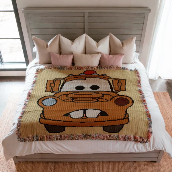 Large C2C crochet blanket featuring Tow Mater from Disney Pixar Cars in pixel art style, with a beige background and colorful fringe border, displayed in a modern living room.