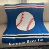 Baseball Intarsia Knit Blanket Pattern - a white baseball with red stitching and a black outline centered on a blue background with a garter stitch border, worked in stockinette intarsia colorwork with 4 colors: Blue, White, Red, Black.