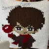 Caleb Finger Knit Blanket Pattern - video game character with dark brown hair holding a red apple, purple outfit and red accents on a white background, worked in stockinette colorwork intarsia with 6 colors: White, Brown, Purple, Red, Powder, Black.