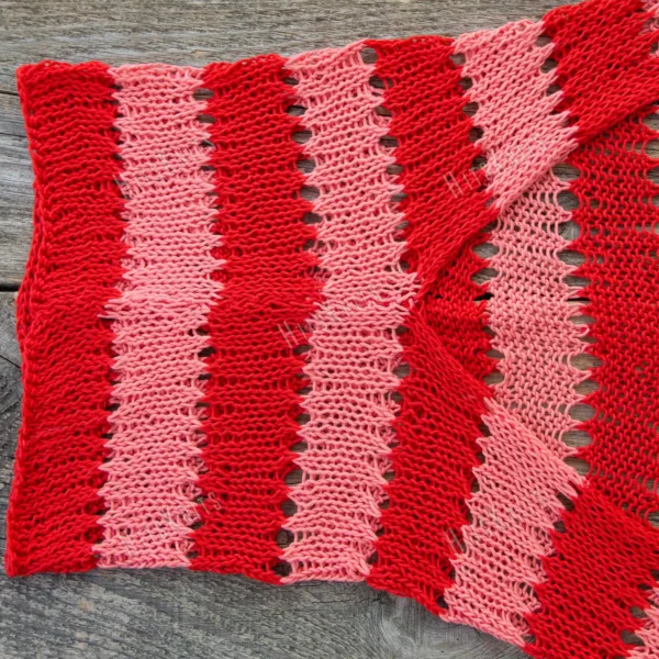 Easy striped lace bolero knitting pattern showing a loose summer shrug worked in thin cotton yarn with lace eyelet rows at each colour change, in coral and red stripes, one size fits most.