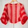 Easy striped lace bolero knitting pattern showing a loose summer shrug worked in thin cotton yarn with lace eyelet rows at each colour change, in coral and red stripes, one size fits most.