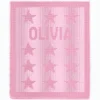 Olivia Blanket Knitting Pattern showing the name Olivia in raised knit and purl lettering with rows of small textured stars, on a solid blush pink blanket with a garter stitch border, worked in one color, 100 stitches x 190 rows.