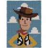 Woody Chunky Blanket Knitting Pattern showing a cowboy character in a wide brown hat with a smiling face and a yellow shirt, on a sky blue background with white clouds, worked in stockinette colorwork with 8 colors: Sky, Ivory, Yellow, Powder, Brown, Black, Camel, and Red.
