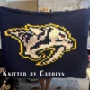 Nashville Predators Finger Knitting Blanket Pattern showing the sabretooth tiger hockey logo in white and navy with a gold outline, gray shading, and an orange eye on a navy background, worked in stockinette colorwork intarsia with 5 colors: Navy, White, Gold, Gray, and Orange.