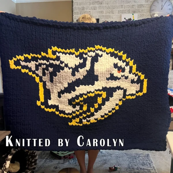 Nashville Predators Finger Knitting Blanket Pattern showing the sabretooth tiger hockey logo in white and navy with a gold outline, gray shading, and an orange eye on a navy background, worked in stockinette colorwork intarsia with 5 colors: Navy, White, Gold, Gray, and Orange.