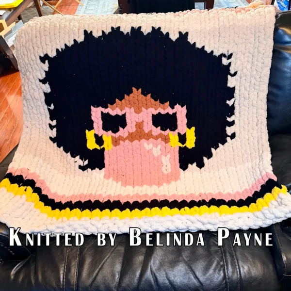 Bubblegum Chunky Blanket Finger Knitting Pattern showing a girl with a black afro, camel skin, pink sunglasses, and gold hoop earrings blowing a pink bubblegum bubble on an ivory background with pink, black, and yellow stripes, worked in stockinette colorwork intarsia with 5 colors: Ivory, Black, Pink, Yellow, and Camel.