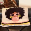 Bubblegum Chunky Blanket Finger Knitting Pattern showing a girl with a black afro, camel skin, pink sunglasses, and gold hoop earrings blowing a pink bubblegum bubble on an ivory background with pink, black, and yellow stripes, worked in stockinette colorwork intarsia with 5 colors: Ivory, Black, Pink, Yellow, and Camel.