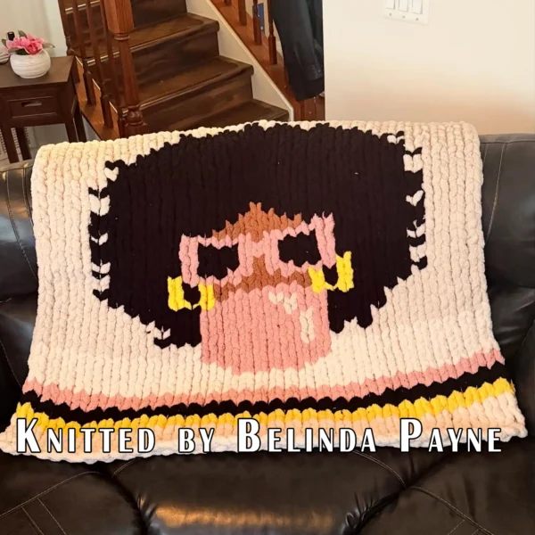 Bubblegum Chunky Blanket Finger Knitting Pattern showing a girl with a black afro, camel skin, pink sunglasses, and gold hoop earrings blowing a pink bubblegum bubble on an ivory background with pink, black, and yellow stripes, worked in stockinette colorwork intarsia with 5 colors: Ivory, Black, Pink, Yellow, and Camel.