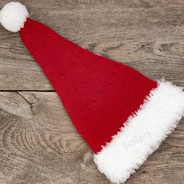 Santa Hat Knitting Pattern showing a long red knitted Santa hat with a soft fluffy white brim and a white pompom, an easy knit and purl Christmas hat for adults.