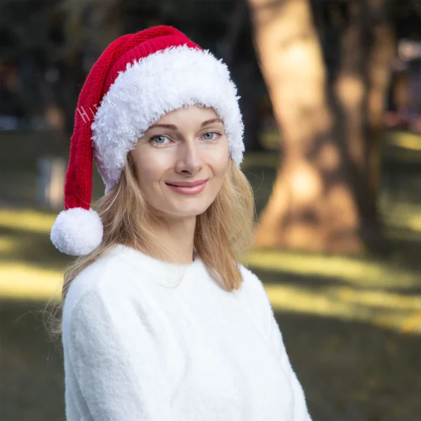 Santa Hat Knitting Pattern showing a long red knitted Santa hat with a soft fluffy white brim and a white pompom, an easy knit and purl Christmas hat for adults.