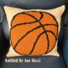 Basketball Intarsia Knit Panel Pattern showing a bold orange basketball pillow with heavy black seam lines on a cream background, worked in stockinette intarsia colorwork with 3 colors: Cream, Orange, and Black.
