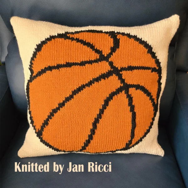 Basketball Intarsia Knit Panel Pattern showing a bold orange basketball pillow with heavy black seam lines on a cream background, worked in stockinette intarsia colorwork with 3 colors: Cream, Orange, and Black.