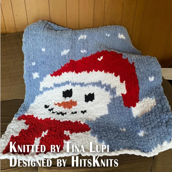 Xmas Snowman Finger Knit Blanket Pattern - a close-up snowman face with a red Christmas hat, red scarf, black coal eyes and smile, and an orange carrot nose, on a spa blue background with white snowflakes, worked in stockinette colorwork intarsia with 5 colors: Spa Blue, White, Red, Black, Carrot.