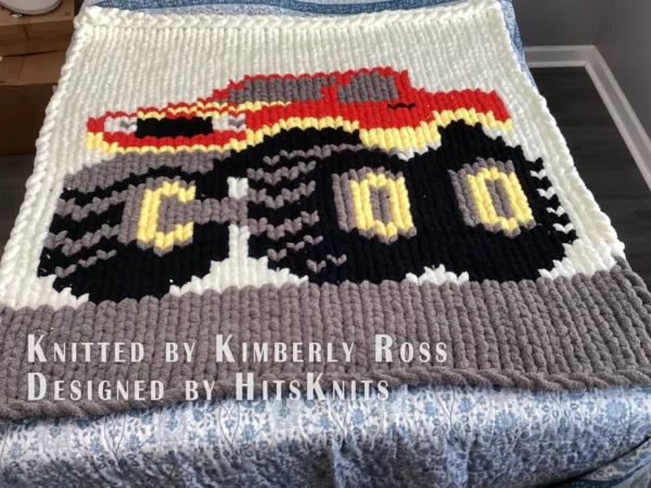 Monster Jam Truck Chunky Blanket Pattern - a bold red monster truck with smoky gray windows, yellow headlights, and three oversized black wheels on a gray track, worked in stockinette colorwork intarsia with 5 colors: Ivory, Gray, Black, Red, Yellow.