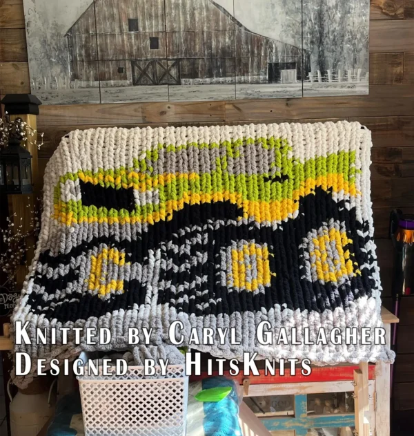 Monster Jam Truck Chunky Blanket Pattern - a bold red monster truck with smoky gray windows, yellow headlights, and three oversized black wheels on a gray track, worked in stockinette colorwork intarsia with 5 colors: Ivory, Gray, Black, Red, Yellow.