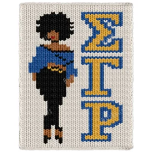 Sigma Gamma Rho Lady Finger Knit Blanket, a standing Black woman with an afro, red lip, blue blouse, black pants and heels beside the greek letters Sigma Gamma Rho, worked in stockinette colorwork intarsia with 6 colors: Ivory, Blue, Black, Gold, Camel, and Red.
