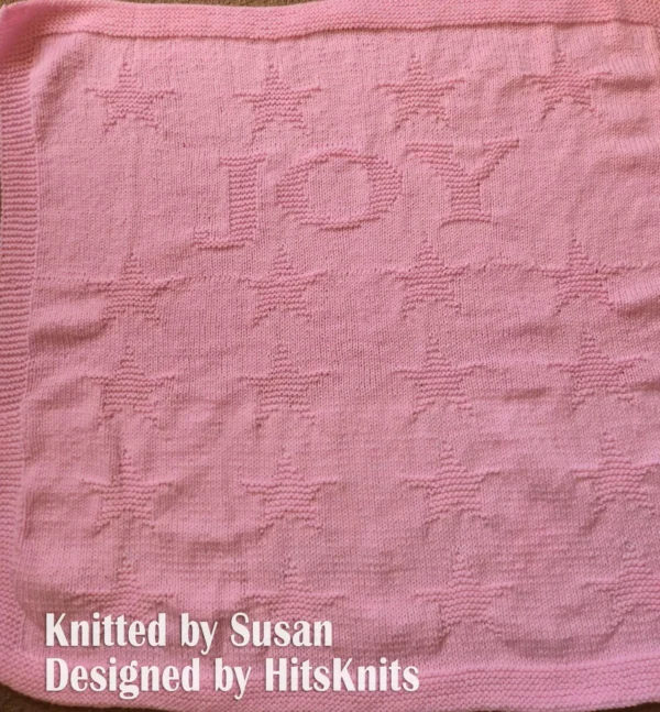 Joy Stars Blanket Knitting Pattern showing a textured silhouette of little stars framing the word Joy, on a solid single-colour blanket with a garter stitch border, worked in one color, 148 stitches x 215 rows.