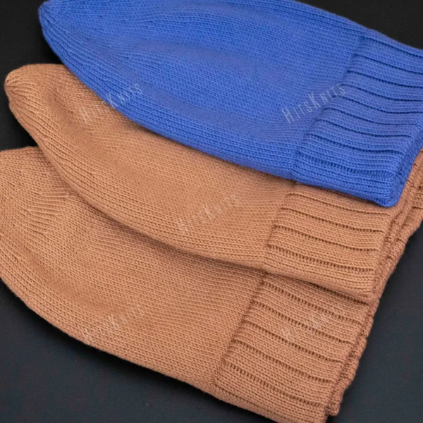 Machine Knitting Slouchy Hat Pattern showing finished cotton beanies in warm brown and royal blue with a mock rib cuff, laid flat and stacked to show the smooth stockinette body, the round crown and the cuff worn down or turned up.