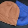 Machine Knitting Slouchy Hat Pattern showing finished cotton beanies in warm brown and royal blue with a mock rib cuff, laid flat and stacked to show the smooth stockinette body, the round crown and the cuff worn down or turned up.
