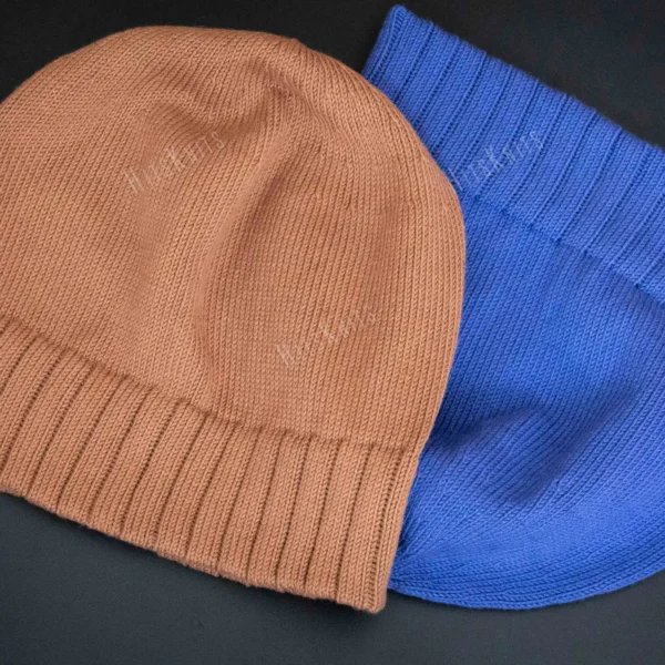 Machine Knitting Slouchy Hat Pattern showing finished cotton beanies in warm brown and royal blue with a mock rib cuff, laid flat and stacked to show the smooth stockinette body, the round crown and the cuff worn down or turned up.