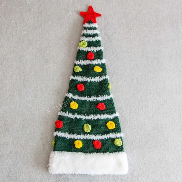 Christmas Tree Hat Knitting Pattern showing a tall dark green knitted beanie with a white fluffy Santa style brim and stripes, yellow, red and green bobbles and a red crochet star on top, knitted flat and seamed, worked in bulky yarn, unisex adult size 56-59 cm.