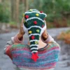 Christmas Tree Hat Knitting Pattern showing a tall dark green knitted beanie with a white fluffy Santa style brim and stripes, yellow, red and green bobbles and a red crochet star on top, knitted flat and seamed, worked in bulky yarn, unisex adult size 56-59 cm.