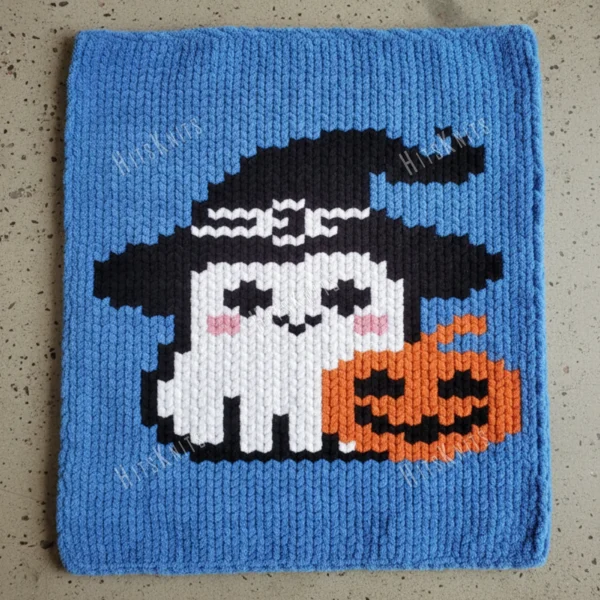 Cute Ghost Witch Hat Throw Knitting Pattern - a smiling white ghost in a black witch hat with pink cheeks sitting beside a carved jack o lantern on a blue night sky, knitted in stockinette colorwork intarsia with 5 colors: Blue, Black, White, Pumpkin, Pink.